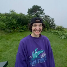 Beck smiles in a backwards hat and purple sweatshirt with green misty landscape.